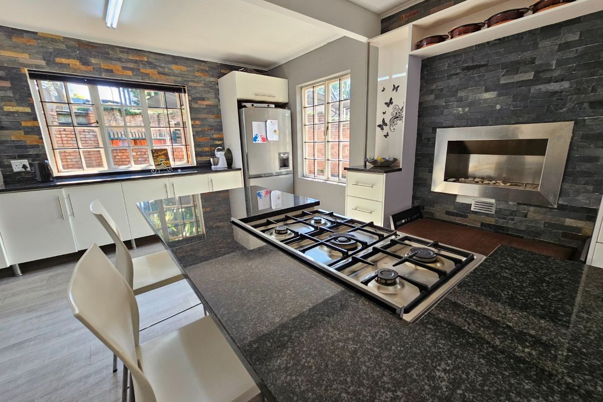 Modern kitchen featuring a central island with a built-in gas hob, granite countertops, stone-clad feature walls, and an integrated fireplace.