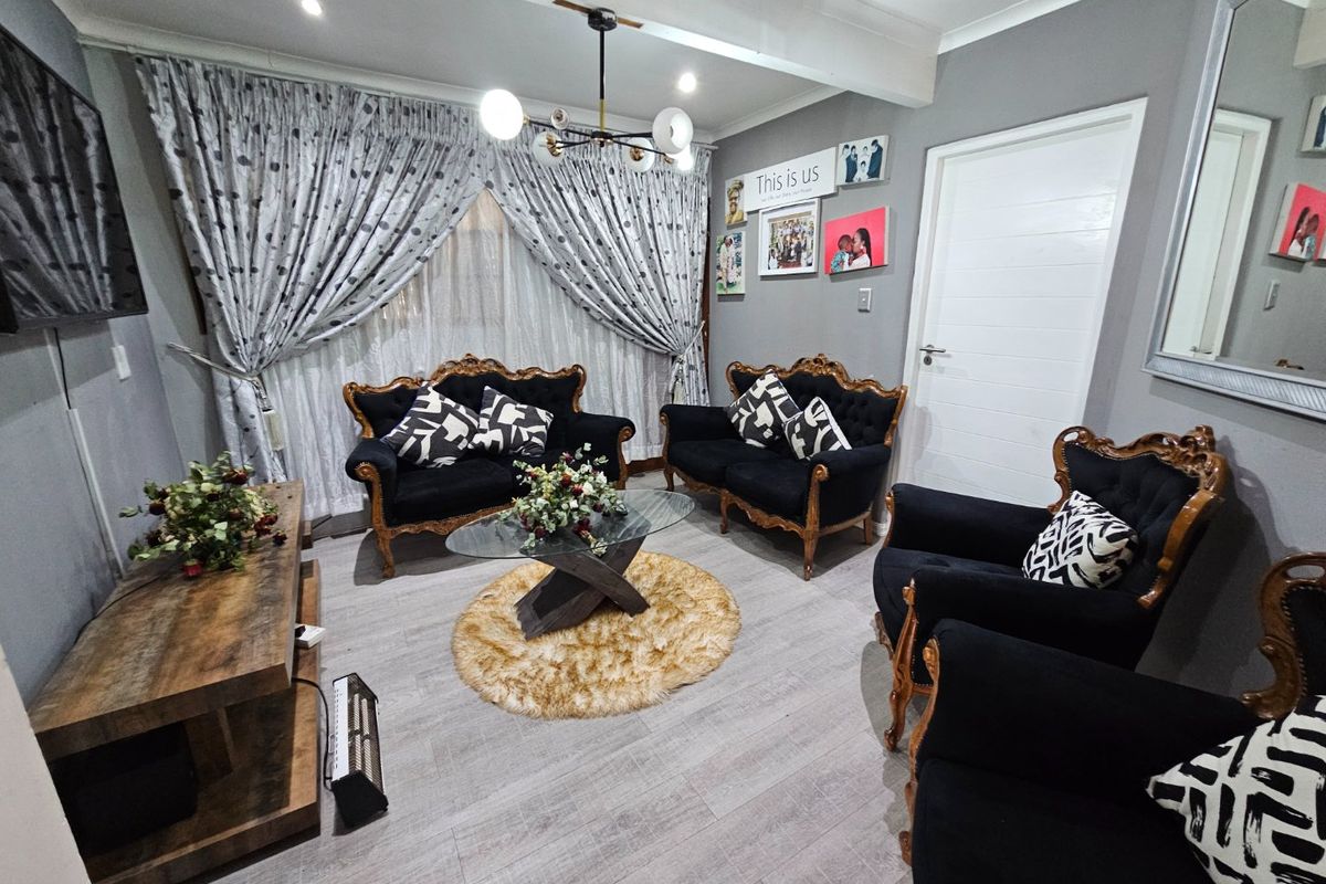 A well-maintained living room featuring modern grey laminate flooring, recessed ceiling lighting, and a contemporary chandelier.