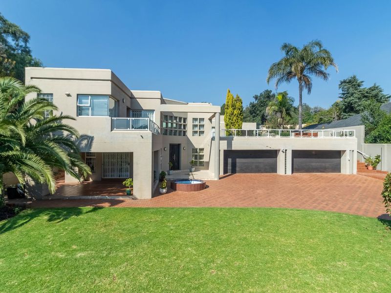 A modern multi-level residential property featuring a spacious paved driveway, double garage, and an elevated balcony overlooking a well-maintained front garden.