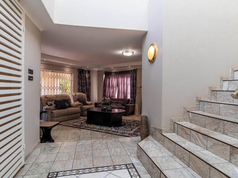 Spacious entrance hall featuring tiled flooring, a staircase with decorative tiles, and a skylight, leading into an open-plan living area.