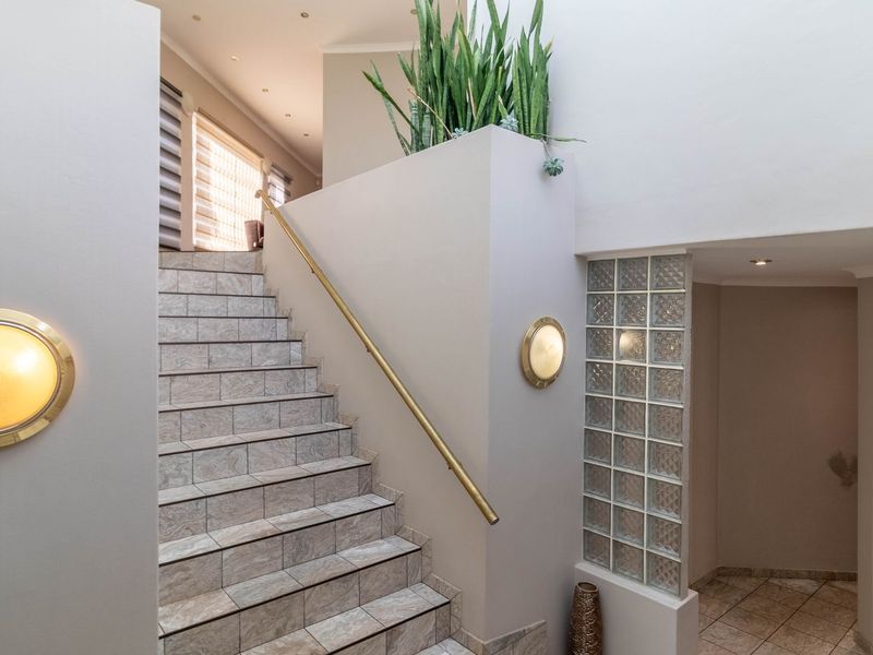A bright entrance foyer featuring a tiled staircase with a metal handrail, decorative glass block wall, and warm wall-mounted lighting.