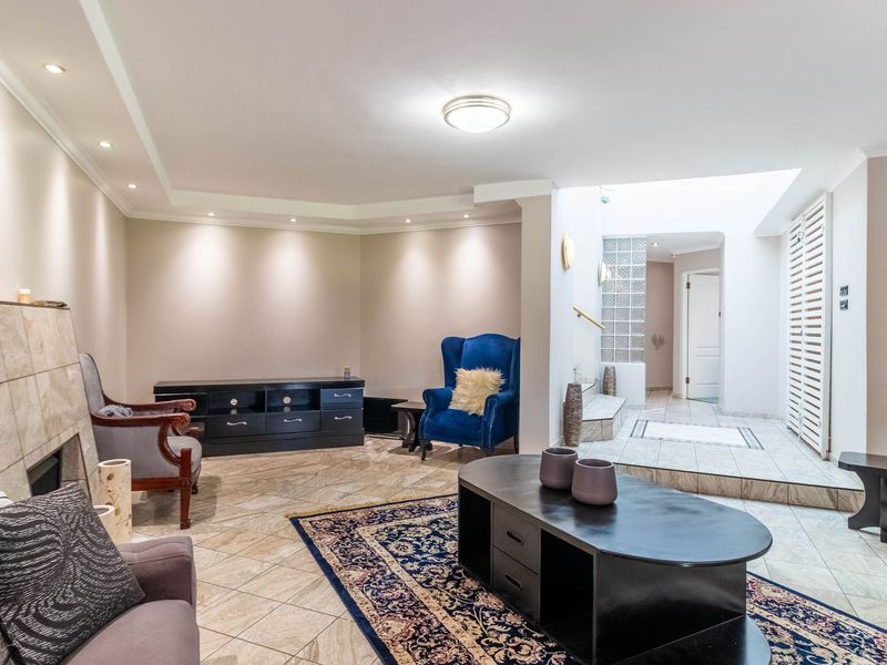 Spacious living room featuring tiled flooring, recessed lighting, a unique glass block wall, and a built-in fireplace with a raised transition area.