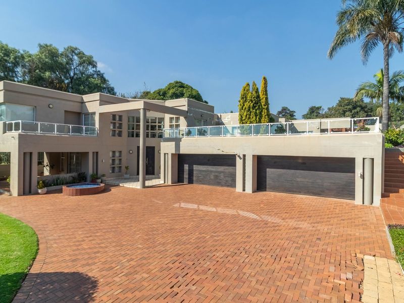 Modern multi-level residence featuring a spacious brick-paved driveway, double garage, and an expansive upper-level balcony with glass balustrades.