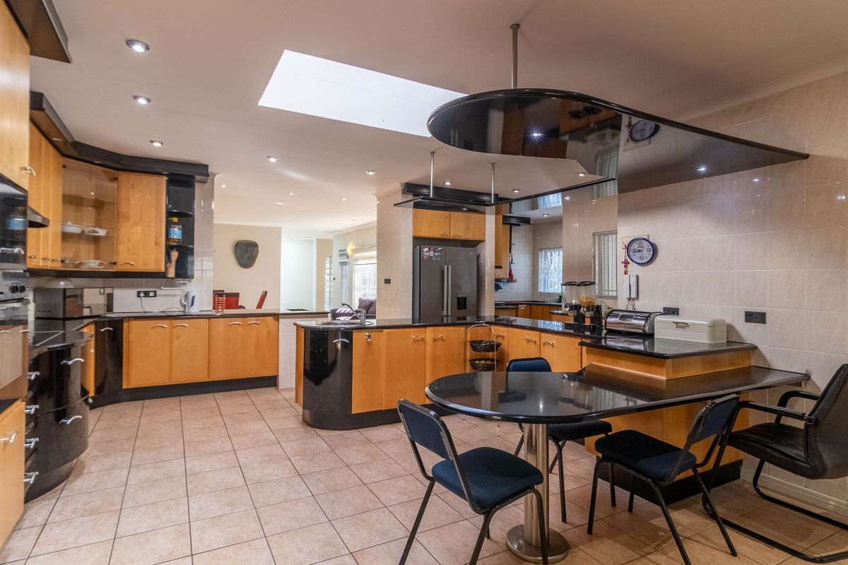Spacious kitchen featuring light wood cabinetry, black granite countertops, a central breakfast bar, integrated appliances, and a large skylight for natural illumination.