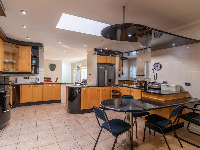 Spacious kitchen featuring light wood cabinetry, black granite countertops, a central breakfast bar, integrated appliances, and a large skylight for natural illumination.