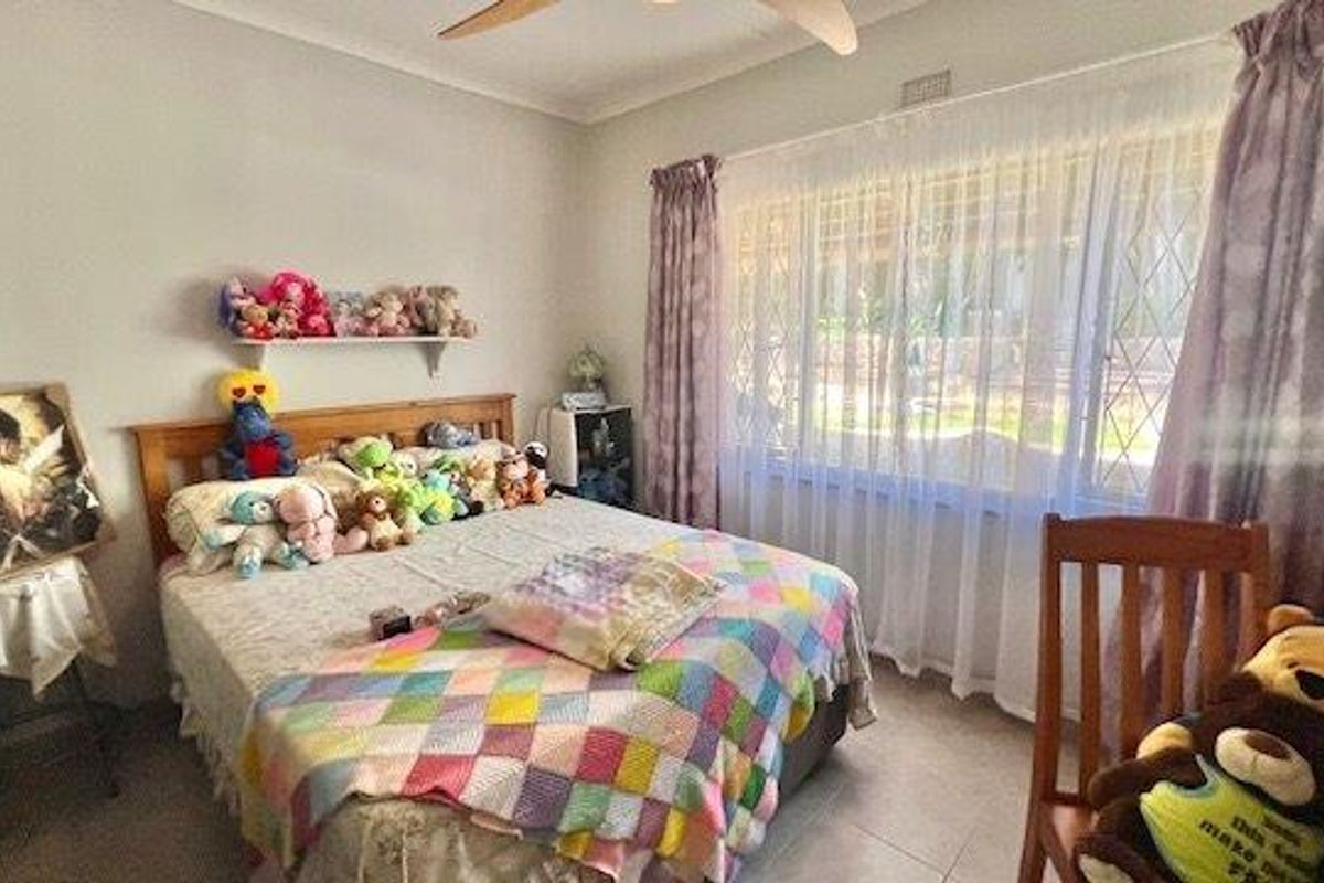 A functional bedroom featuring tiled flooring, a ceiling fan, and a large window fitted with security bars.