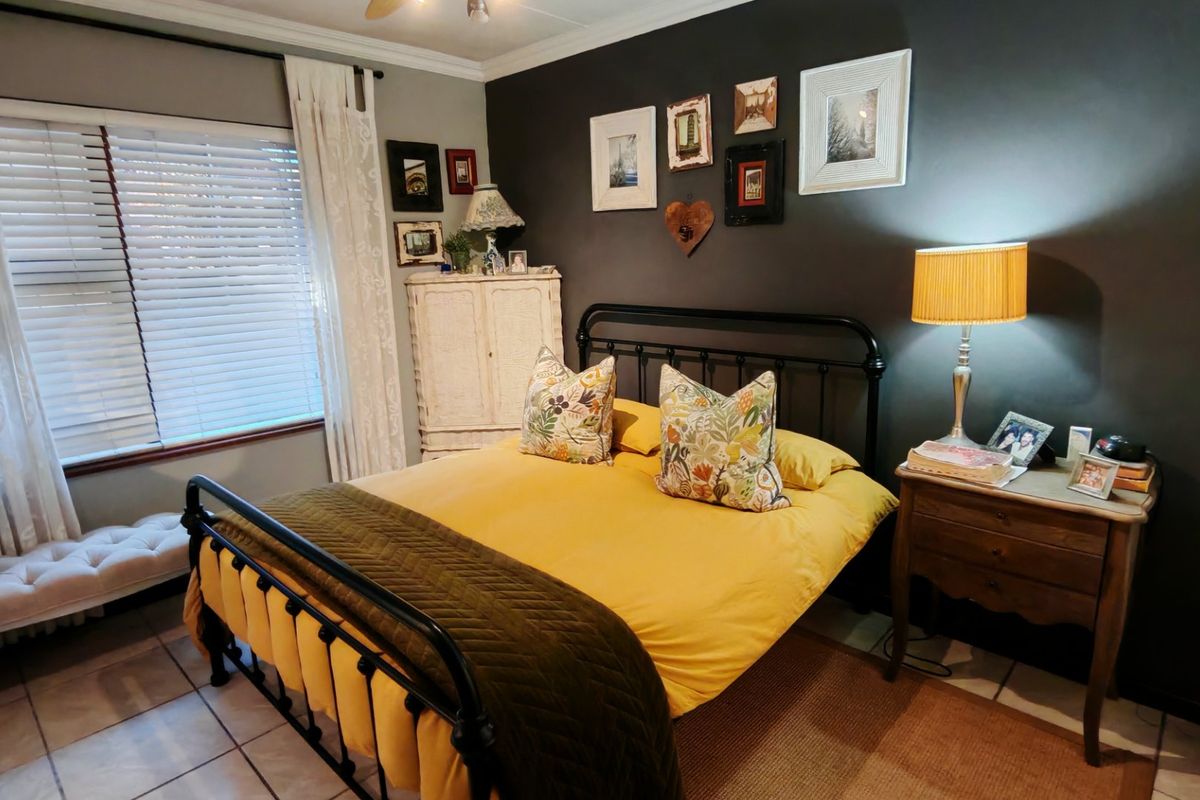 A cozy bedroom featuring tiled flooring, a ceiling fan, and venetian blinds, with a dark accent wall creating a warm atmosphere.