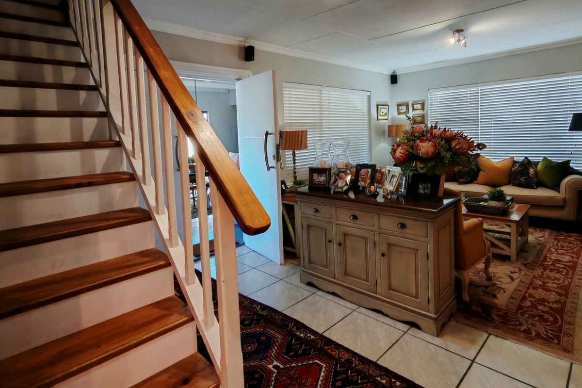 A well-maintained living area featuring a staircase with a wooden handrail, tiled flooring, and natural light filtered through venetian blinds.