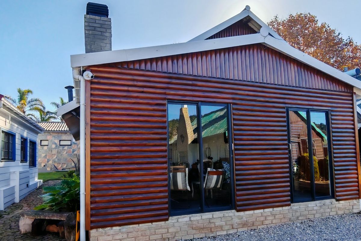 Rear view of a house featuring timber log-style cladding, a brick chimney, and modern sliding glass doors set on a brick foundation.