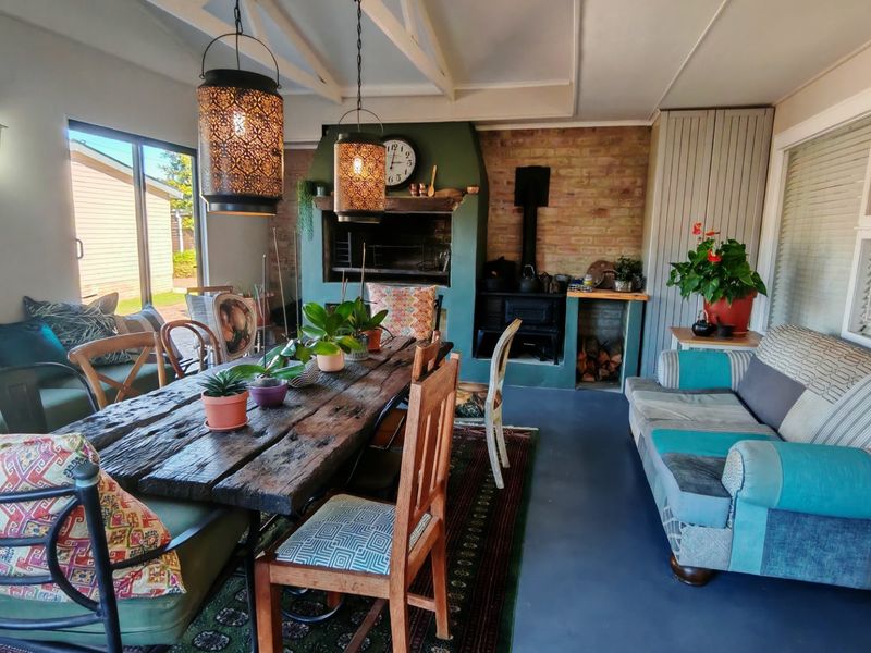 A spacious covered patio featuring a built-in braai, wood-burning stove, exposed beam ceiling, and large sliding doors leading to the garden.