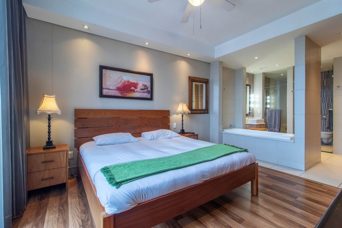 Spacious bedroom featuring laminate flooring, recessed lighting, and an open-plan en-suite bathroom with a built-in bathtub and glass partition.
