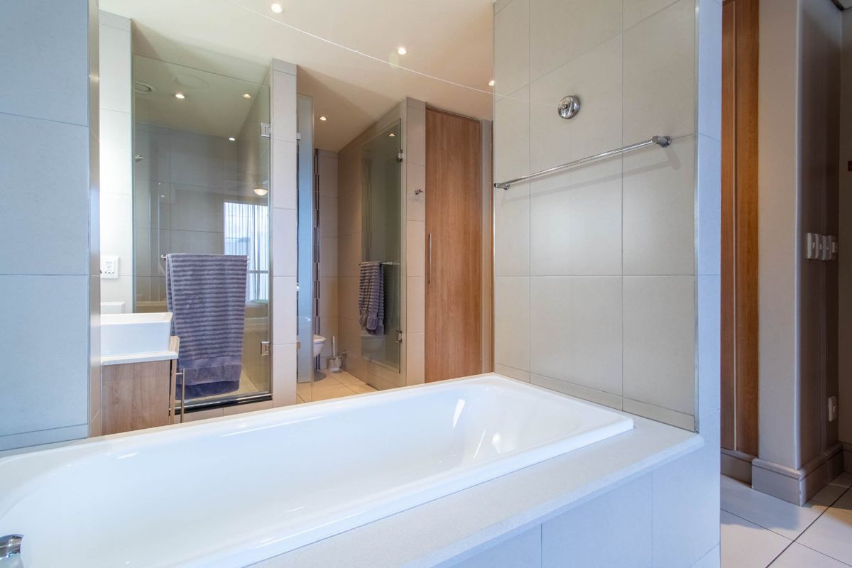 Modern bathroom featuring a built-in bathtub, a separate glass-enclosed shower, neutral wall tiling, and contemporary vanity cabinetry.