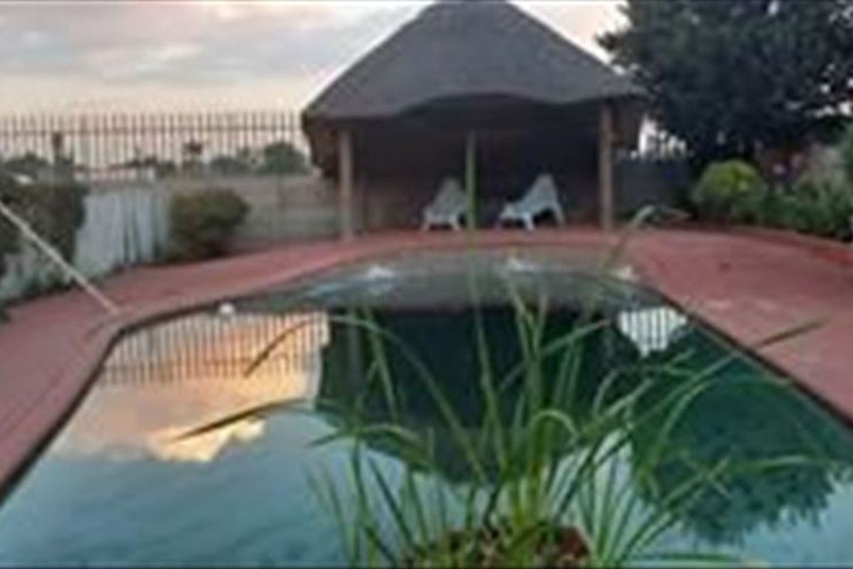 Outdoor pool area featuring a swimming pool with surrounding paved decking and a covered thatch lapa structure.
