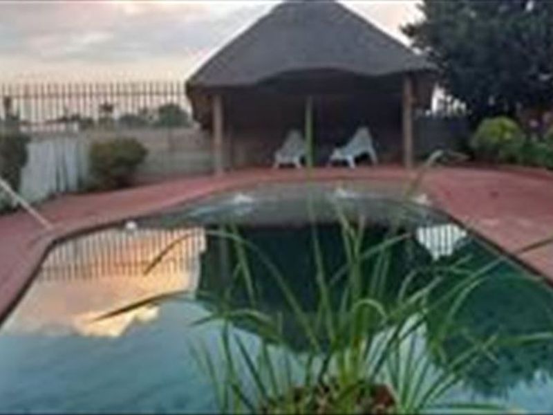 Outdoor pool area featuring a swimming pool with surrounding paved decking and a covered thatch lapa structure.