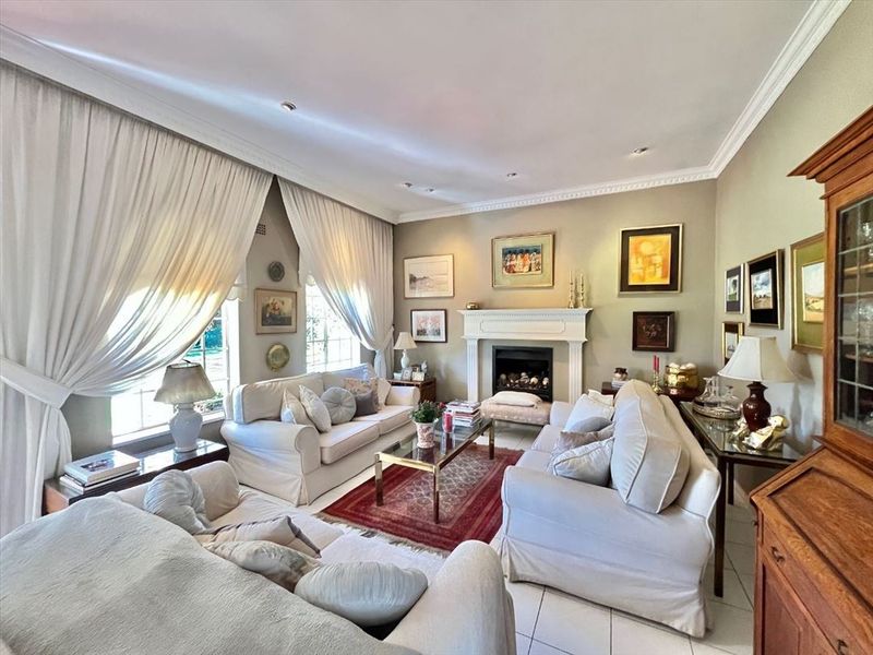A well-maintained living room featuring a classic fireplace with a mantelpiece, crown molding, recessed lighting, and neutral tiled flooring.