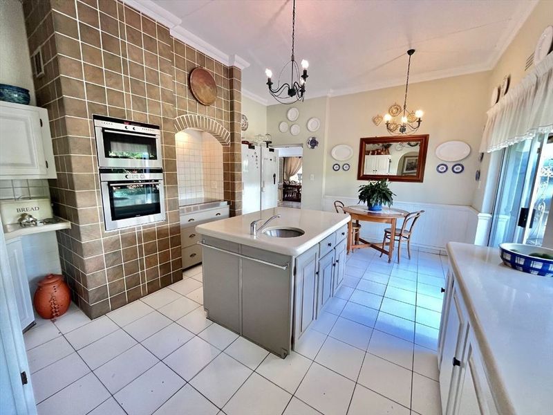 Spacious kitchen featuring a central island with sink, built-in double oven, tiled splashback, and classic wainscoting detail.