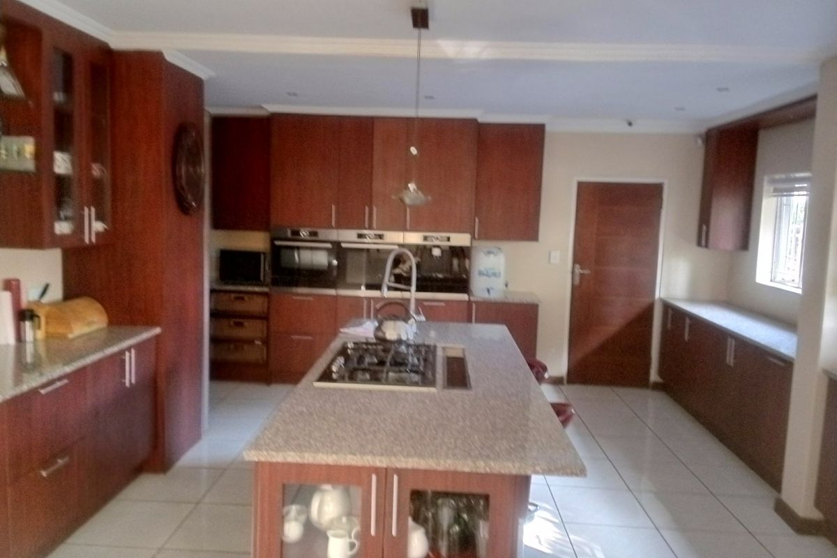 Spacious kitchen featuring dark wood cabinetry, granite countertops, a central island with a gas hob, and tiled flooring.