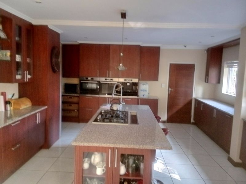 Spacious kitchen featuring dark wood cabinetry, granite countertops, a central island with a gas hob, and tiled flooring.