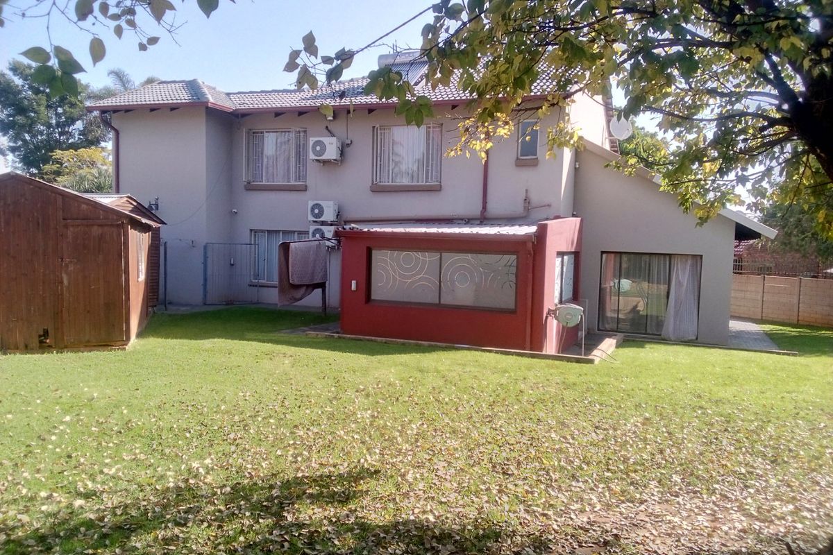 Rear view of a two-story house featuring a garden, lawn, and a detached shed, with visible air conditioning units and solar water heating infrastructure.