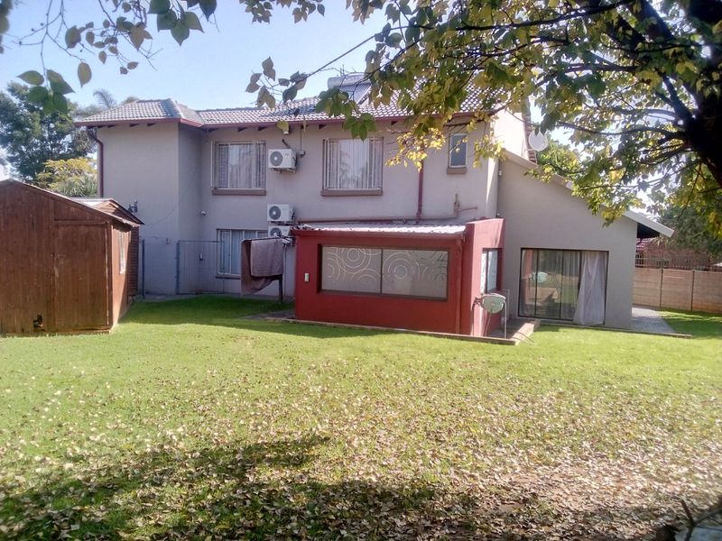 Rear view of a two-story house featuring a garden, lawn, and a detached shed, with visible air conditioning units and solar water heating infrastructure.