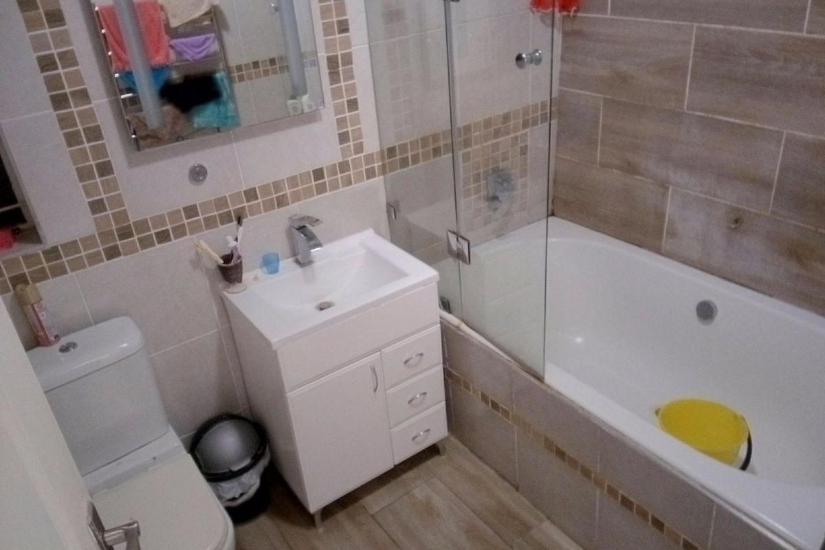 A functional bathroom featuring a vanity unit with basin, a toilet, and a bathtub with a glass shower screen and tiled finishes.