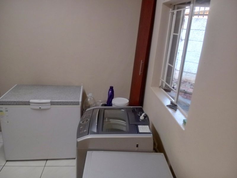 A functional laundry area featuring tiled flooring and a window with security bars, providing space for utility appliances.