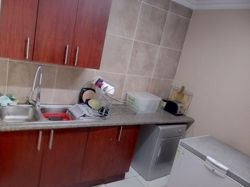 A functional scullery area featuring laminate cabinetry, a stainless steel double sink, tiled splashbacks, and space for laundry or kitchen appliances.