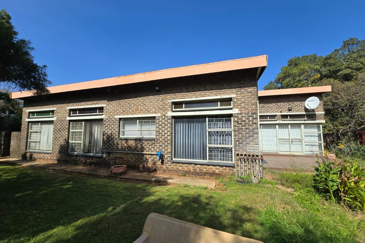 Rear view of a facebrick house featuring aluminium window frames, security bars, and a paved patio area overlooking the garden.