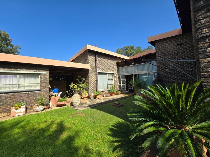 Rear view of the property featuring a brick facade, covered patio area, and a well-maintained lawn with established garden beds.