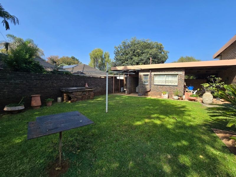 A private rear garden featuring a lawn, a built-in stone braai area, and a covered patio space.