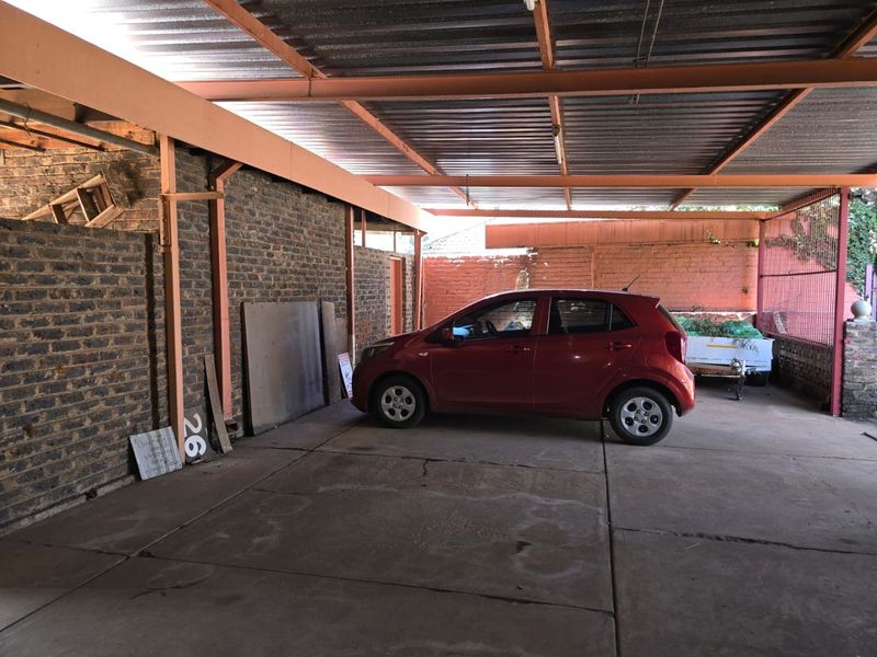 A covered carport or garage area featuring exposed brick walls, a corrugated metal roof, and concrete flooring.