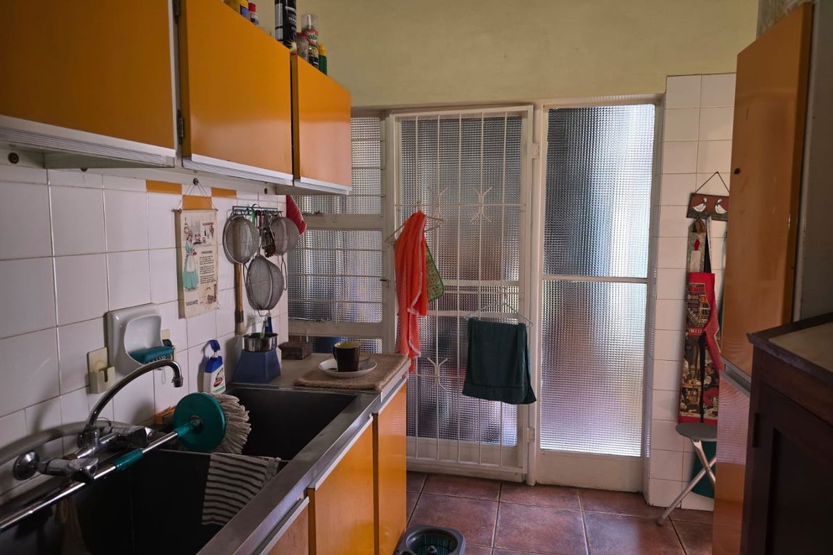 A dated kitchen featuring original cabinetry, tiled backsplash, and a stainless steel sink, with direct access to an exterior security door.