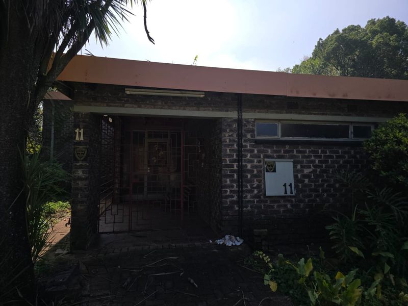 Front elevation of a single-story house featuring exposed brickwork, a flat roof, and a secure gated entrance.