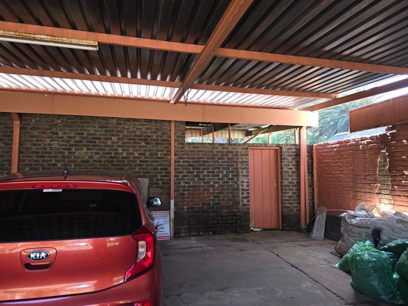 A covered carport or garage area featuring exposed brick walls, a corrugated metal roof, and concrete flooring, providing basic vehicle shelter.