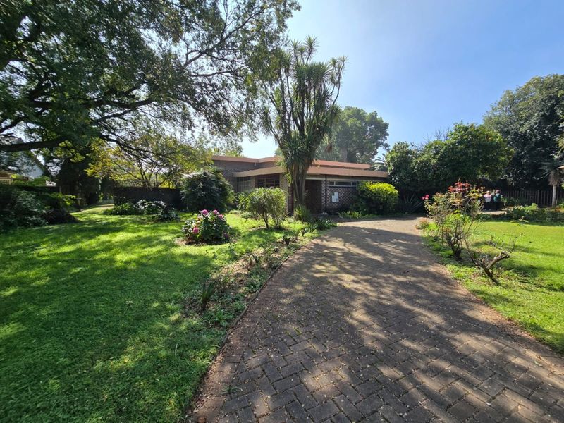 A front view of the property featuring a brick paved driveway leading to the house, surrounded by a mature, well-established garden.
