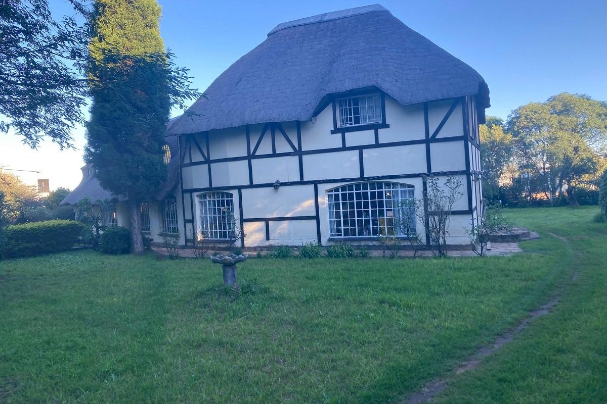 A rear view of a charming cottage-style house featuring a traditional thatched roof, timber-framed walls, and large grid windows set within a spacious garden.