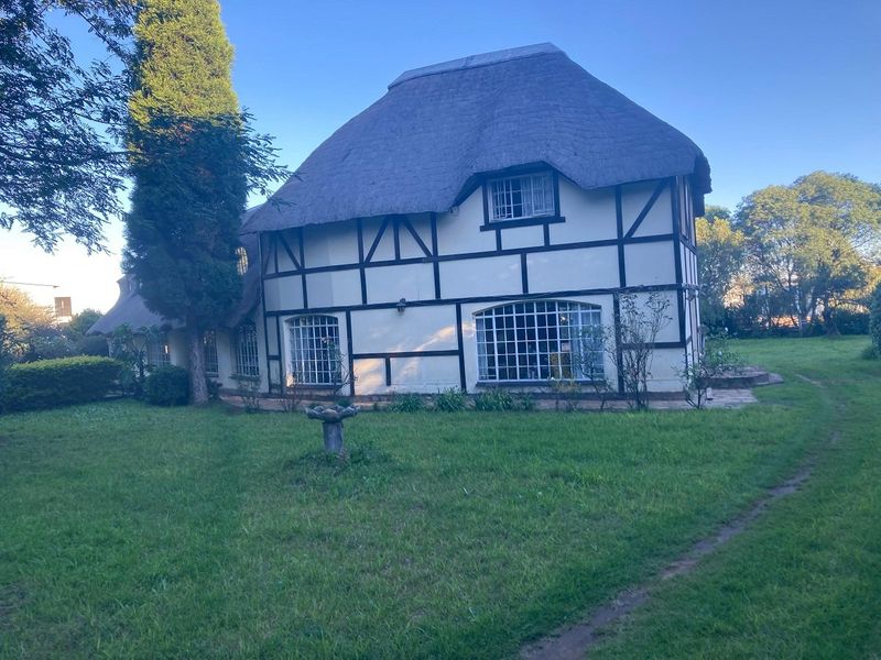 A rear view of a charming cottage-style house featuring a traditional thatched roof, timber-framed walls, and large grid windows set within a spacious garden.