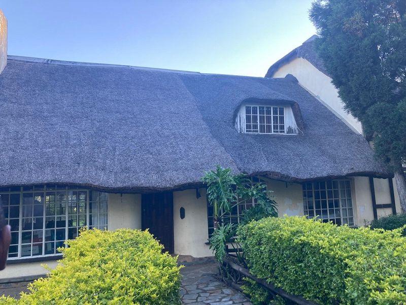 Front facade of a traditional thatched-roof cottage featuring lattice windows, a stone pathway, and established garden landscaping.