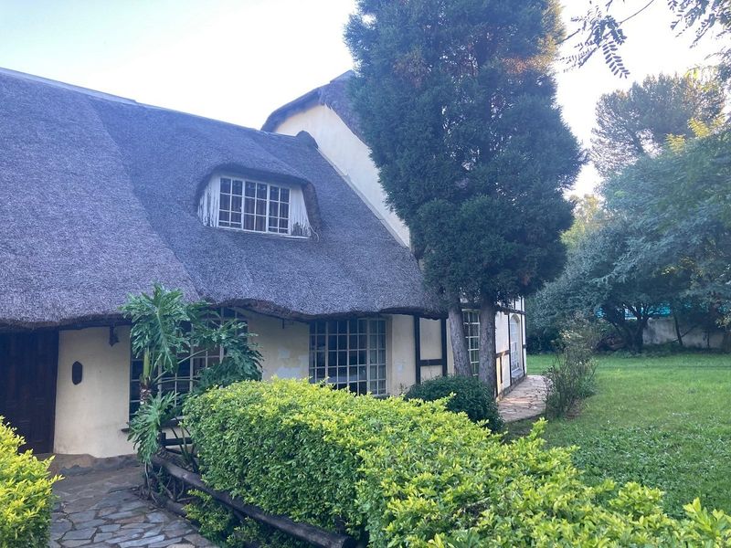 A charming cottage-style home featuring a traditional thatched roof, timber-framed detailing, and a stone pathway leading to the entrance.