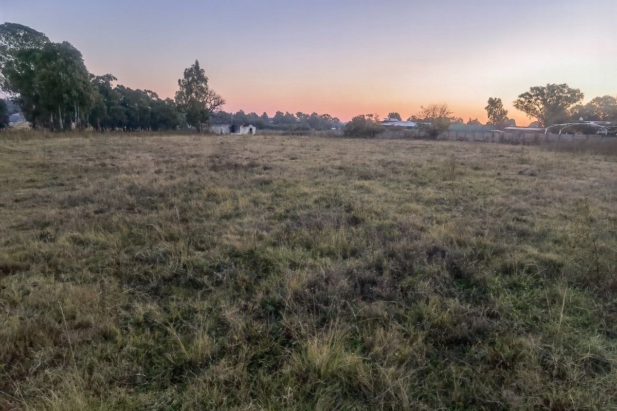 A large, undeveloped plot of land featuring open grass fields and perimeter fencing at sunset.
