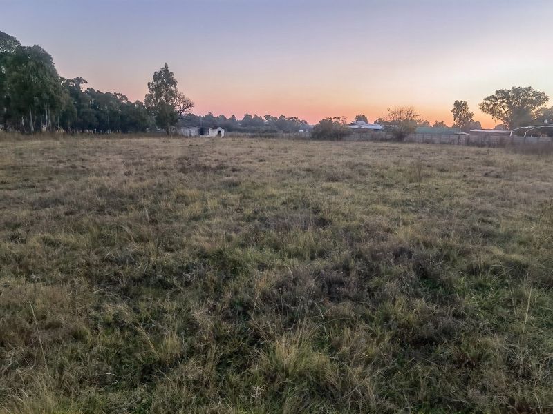 A large, undeveloped plot of land featuring open grass fields and perimeter fencing at sunset.