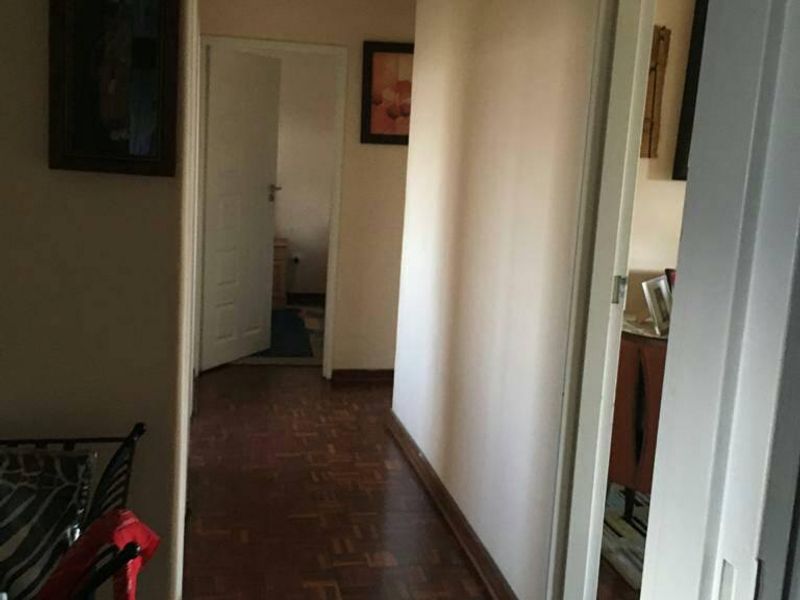 A narrow residential hallway featuring traditional parquet flooring and access to multiple rooms, requiring cosmetic updates to improve the overall aesthetic.