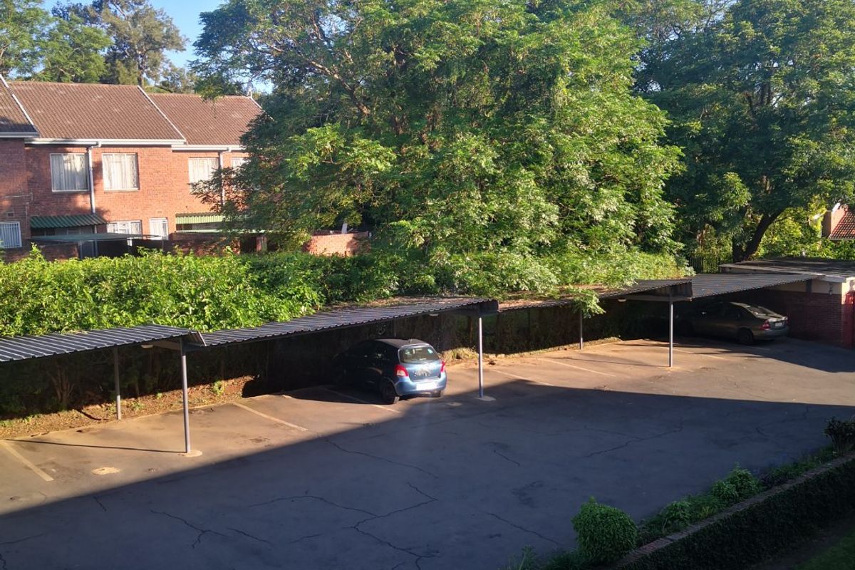 An elevated view of a residential parking area featuring covered carports, asphalt paving, and established perimeter landscaping.