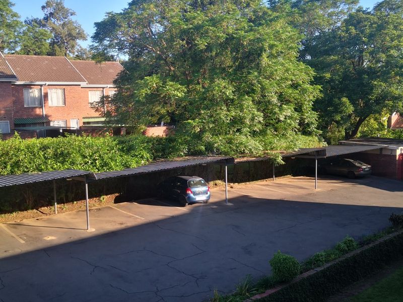 An elevated view of a residential parking area featuring covered carports, asphalt paving, and established perimeter landscaping.