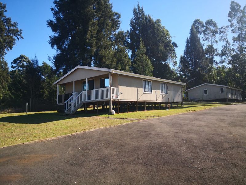 A detached single-story dwelling featuring a raised timber deck, staircase, and asphalt driveway, set within a spacious, tree-lined property.