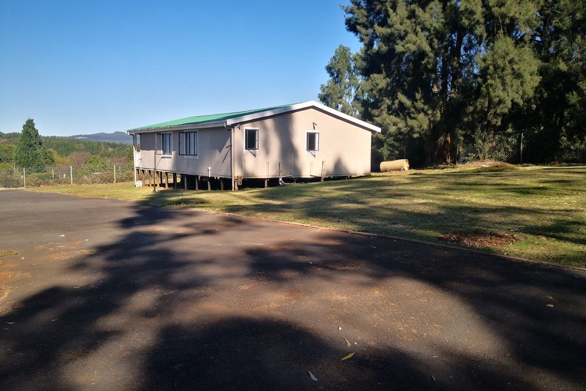 A view of the rear elevation of a house elevated on stilts, featuring a metal roof, set on a large plot with an asphalt driveway.