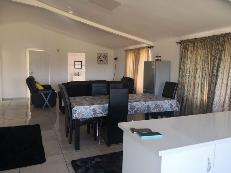 Spacious open-plan living and dining area featuring tiled flooring, a vaulted ceiling, and a central kitchen island, offering a versatile layout for modern living.
