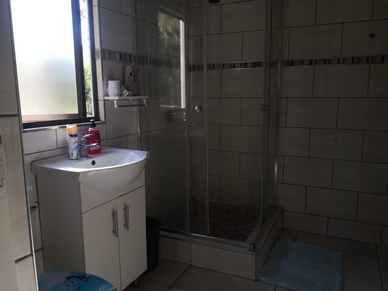 A functional bathroom featuring a vanity cabinet with a washbasin, a glass-enclosed shower, and neutral wall tiling.