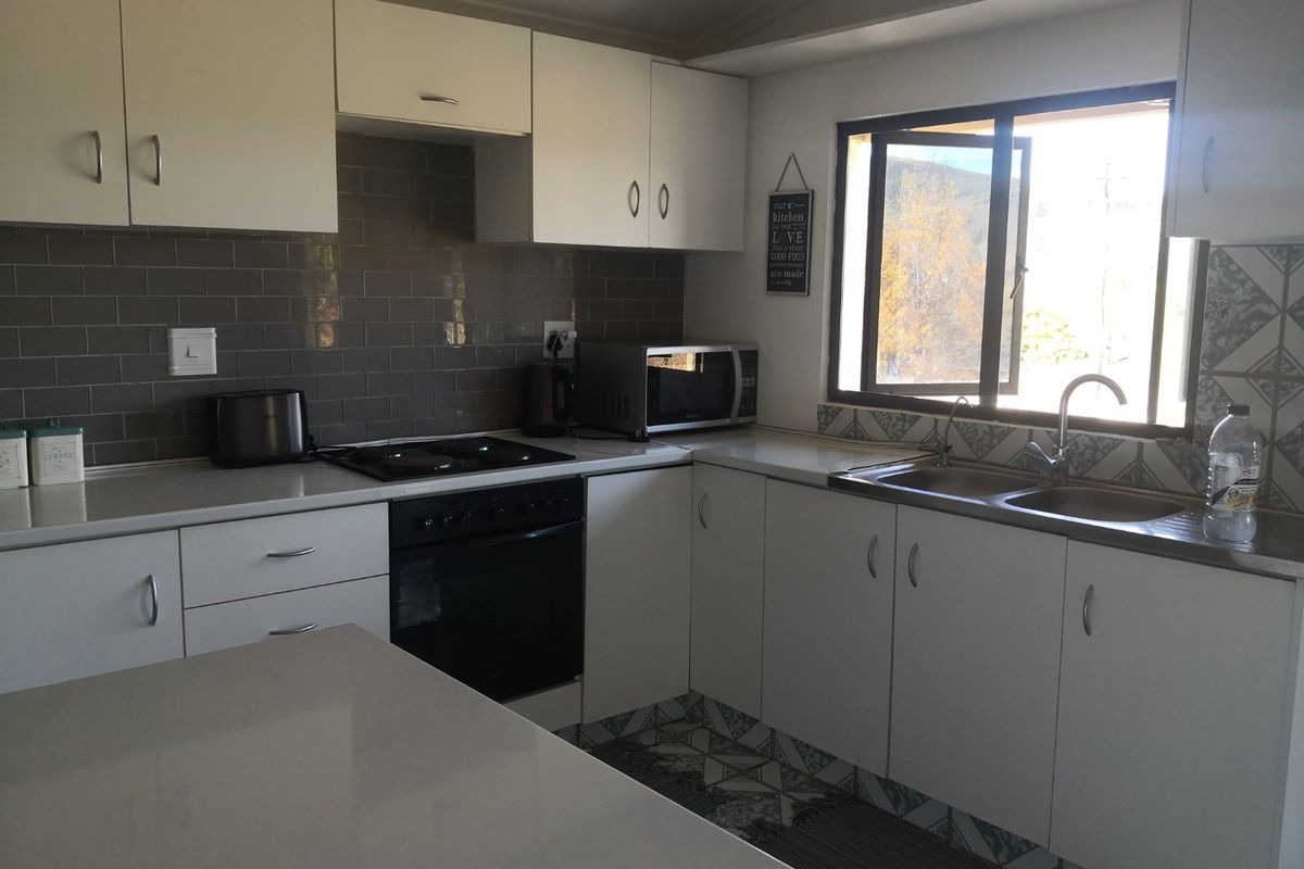 A functional kitchen featuring white cabinetry, subway tile backsplash, built-in oven with hob, and a double bowl sink with natural light.
