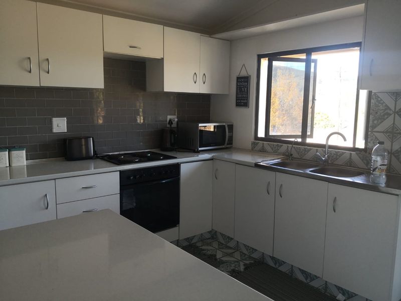 A functional kitchen featuring white cabinetry, subway tile backsplash, built-in oven with hob, and a double bowl sink with natural light.